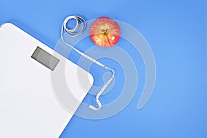 Dieting concept with scale, measuring tape and apple on blue background