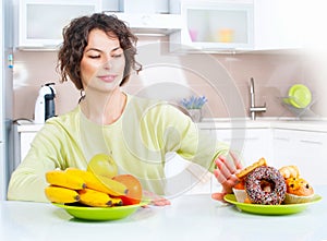 Dieting concept. Young woman choosing between fruits and sweets