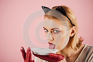 Dieting and health. Girl in kitten ears and red gloves with yoghurt on pink background. cat woman lick milk from