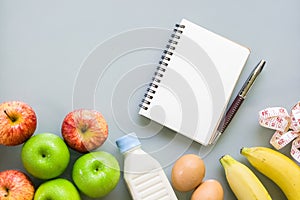 Dieting, healthy and active lifestyles Concept, apples, bananas, egges, tape measure, bottle of milk, blank notebook on grey back