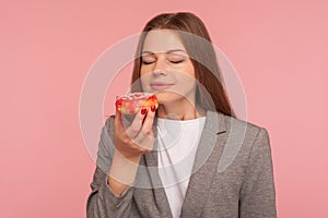 Dieting and junk food. Portrait of hungry woman, office worker in business suit smelling sweet doughnut