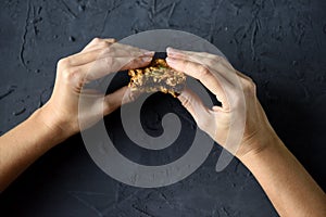Dieting or vegan food concept. Slender woman hands holding oatmeal breakfast cookie sandwich with dark chocolate on black