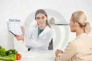 Dietitian in white coat holding meal plan and patient at table