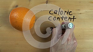 Dietologist hand writes down caloric content of orange on wooden surface