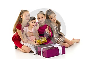 Different age girls are sitting on the floor near gifts. Isolated over white background.