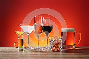 Different alcohol drinks on wooden table against red background