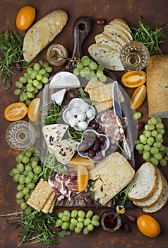 Different appetizers on the board: cheese, prosciutto, ham, bread, olives, grapes