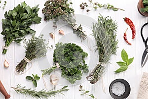 Different aromatic herbs, spool of thread and scissors on white wooden table, flat lay