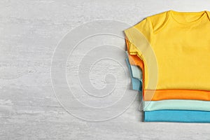 Different baby bodysuits on wooden background, top view. Space for photo