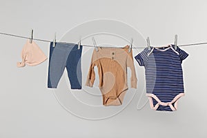 Different baby clothes drying on laundry line against light background