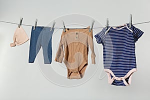 Different baby clothes drying on laundry line against light background