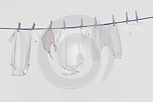 Different baby clothes drying on laundry line against light background