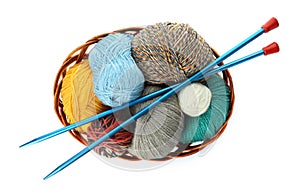 Different balls of woolen knitting yarns and needles in wicker basket on white background, top view
