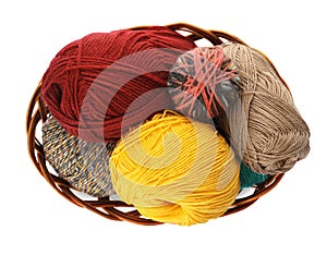 Different balls of woolen knitting yarns in wicker basket on white background, top view