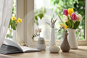 Different beautiful spring flowers, burning candle and book on window sill