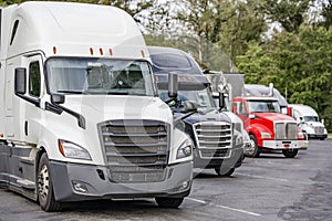 Different big rig industrial pro semi trucks with loaded semi trailers standing in row on the rest area truck stop parking lot