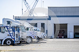 Different big rig semi trucks standing in row on industrial parking lot waiting for maintenance and repair in mechanical workshop