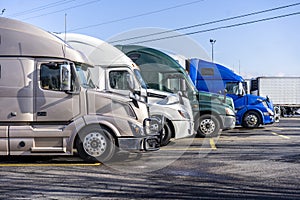 Different big rig semi trucks standing in row on truck stop ready to go