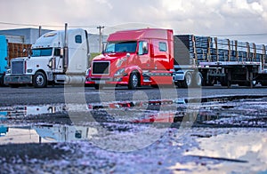 Different big rigs semi trucks with commercial cargo on semi trailers standing on the parking lot in row