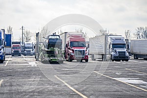 Different big rigs semi trucks with different semi trailers with cargo standing in row on truck stop