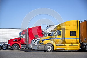 Different big rigs semi trucks with semi trailers standing in row on truck stop parking lot for truck drivers rest and adherence