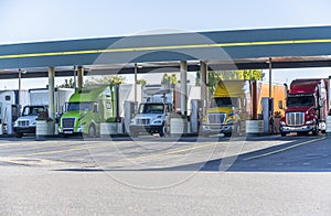 Different big rigs semi trucks standing on fuel station for truck refueling and continuation of the route