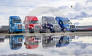 DIfferent big rigs semi trucks standing in row on the parking lot with reflection in water after the rain