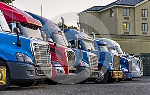 Different big rigs semi trucks standing in row on truck stop for rest at night time