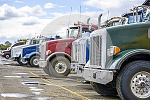 Different big rigs semi trucks tractors standing in row on the warehouse parking lot waiting for next loads for delivery