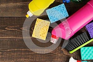 Different bottles with cleaning products and detergents and washcloths in a blue bucket on a brown wooden table. top view