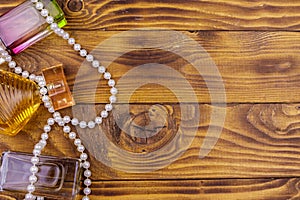 Different bottles of perfume and pearl necklace on wooden background. Top view, copy space