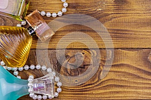 Different bottles of perfume and pearl necklace on wooden background. Top view, copy space