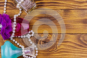 Different bottles of perfume and pearl necklace on wooden background. Top view, copy space