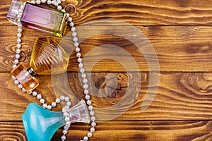 Different bottles of perfume and pearl necklace on wooden background. Top view, copy space