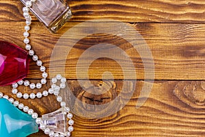 Different bottles of perfume and pearl necklace on wooden background. Top view, copy space