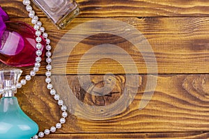 Different bottles of perfume and pearl necklace on wooden background. Top view, copy space