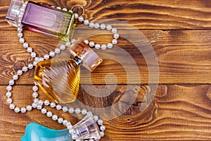 Different bottles of perfume and pearl necklace on wooden background. Top view, copy space