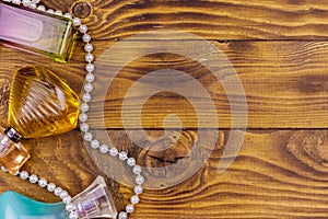 Different bottles of perfume and pearl necklace on wooden background. Top view, copy space