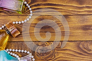 Different bottles of perfume and pearl necklace on wooden background. Top view, copy space