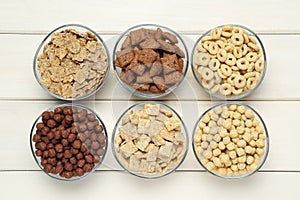 Different breakfast cereals in glass bowls on wooden table, flat lay