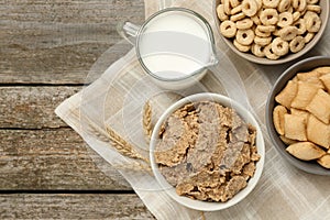 Different breakfast cereals, milk and spikelets on wooden table, flat lay. Space for text