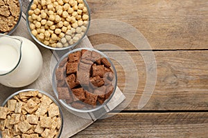 Different breakfast cereals and milk on wooden table, flat lay. Space for text