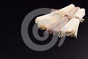 Different bundles raw noodles on black striped mat background with copy space, top view.