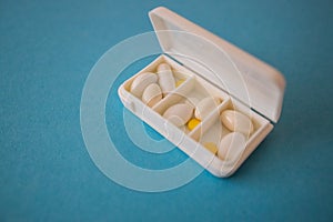 different capsules lie in a white open pill box on a blue background. View from above