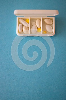 different capsules lie in a white open pill box on a blue background. View from above