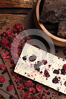 Different chocolate bars with freeze dried fruits on wooden table, flat lay