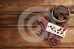 Different chocolate bars with freeze dried fruits on wooden table, flat lay. Space for text