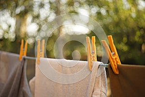 Different clothes are dried on a rope with yellow clothespins in a summer garden. Close up, blurred natural background