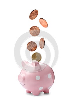 Different coins falling into cute piggy bank on white background