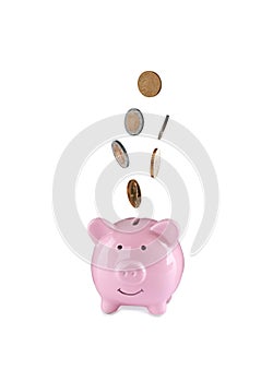 Different coins falling into cute piggy bank on white background